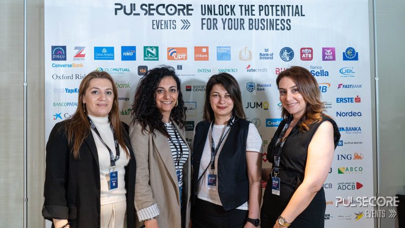 Four delegates pose in front of the PulseCore sponsor wall at a previous PulseCore event