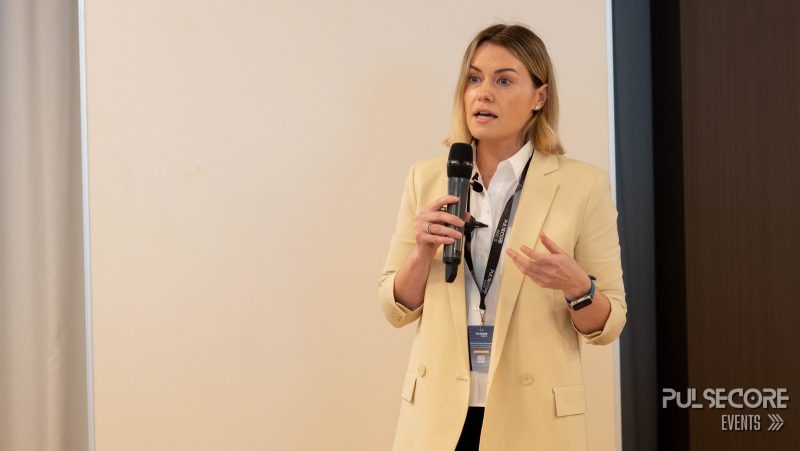 A speaker with a microphone addresses the audience at a previous PulseCore event