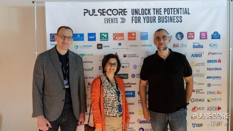 Three delegates pose in front of the PulseCore sponsor wall at a previous PulseCore event